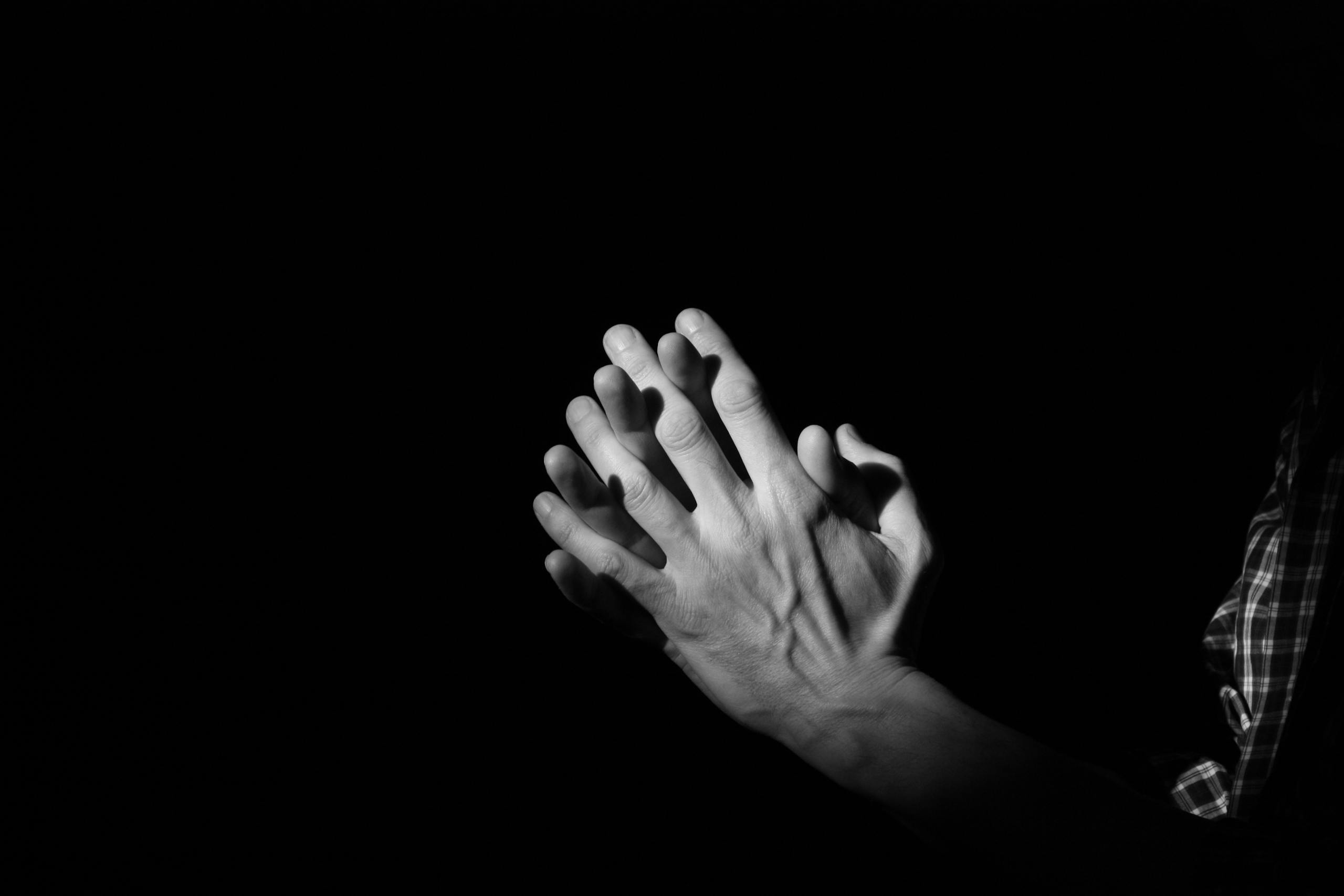 A dramatic black and white photo showing hands clasped in prayer, symbolizing faith and devotion.