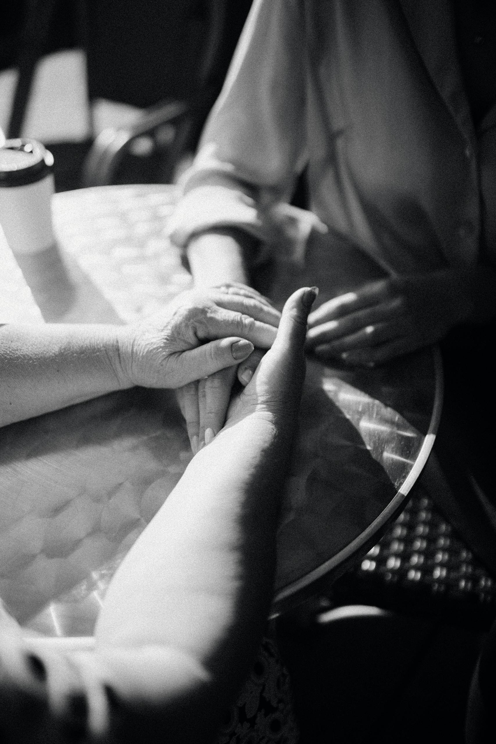Emotive black and white close-up photograph of hands holding on a table, expressing affection.